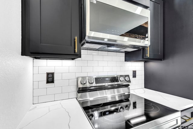 kitchen with tasteful backsplash, appliances with stainless steel finishes, light stone countertops, and dark cabinets