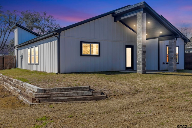 rear view of house featuring board and batten siding, a yard, and fence