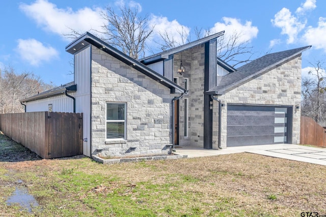 view of front facade with an attached garage, fence, stone siding, and driveway