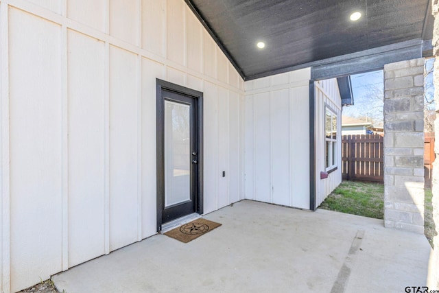 view of exterior entry featuring fence, a patio area, and board and batten siding