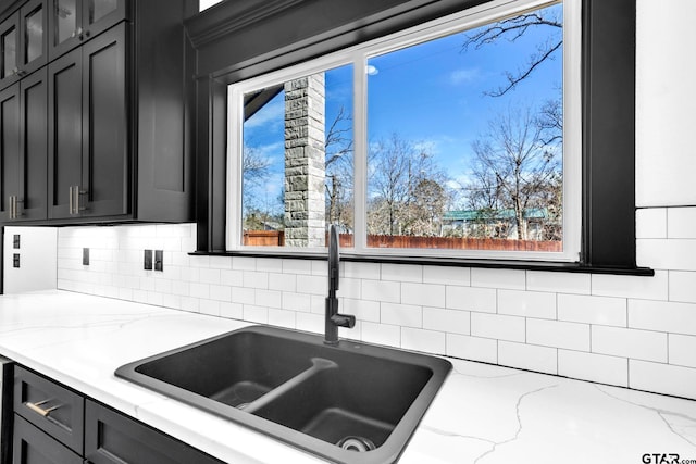 kitchen with dark cabinets, light stone countertops, glass insert cabinets, and a sink