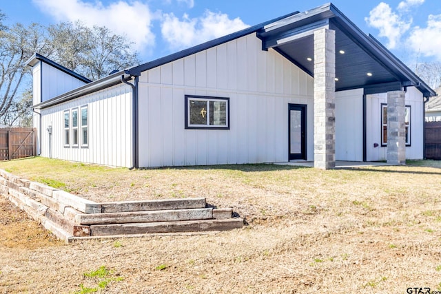 rear view of property featuring board and batten siding, a yard, and fence