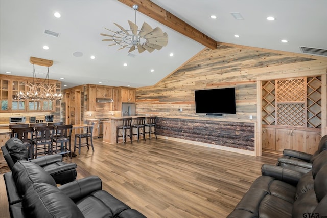 living room with wood walls, ceiling fan with notable chandelier, vaulted ceiling with beams, and light hardwood / wood-style flooring