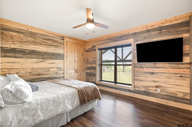 bedroom with dark wood-type flooring, ceiling fan, and wood walls