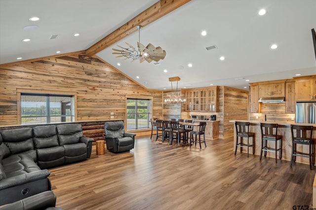 living room with wooden walls, wood-type flooring, ceiling fan with notable chandelier, and beam ceiling