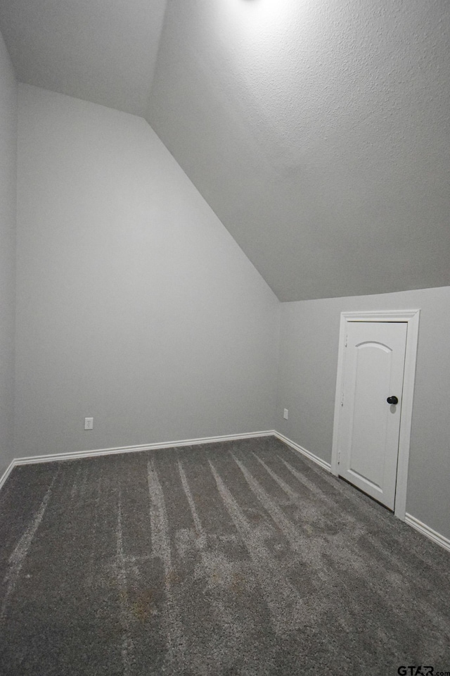 additional living space featuring baseboards, dark carpet, vaulted ceiling, and a textured ceiling