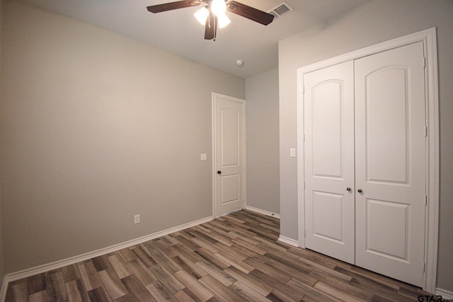 unfurnished bedroom with dark wood-style floors, a closet, visible vents, ceiling fan, and baseboards