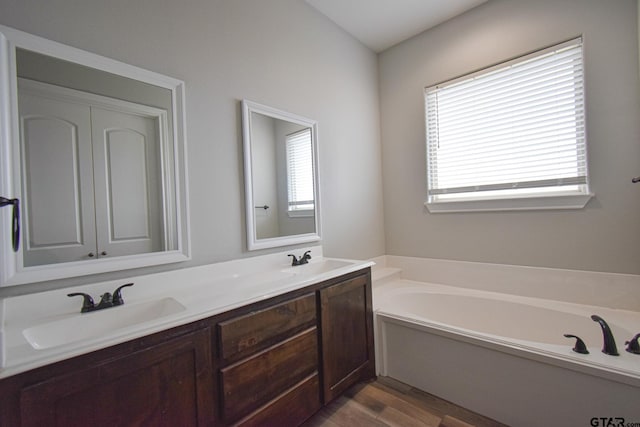 full bathroom with a garden tub, double vanity, wood finished floors, and a sink