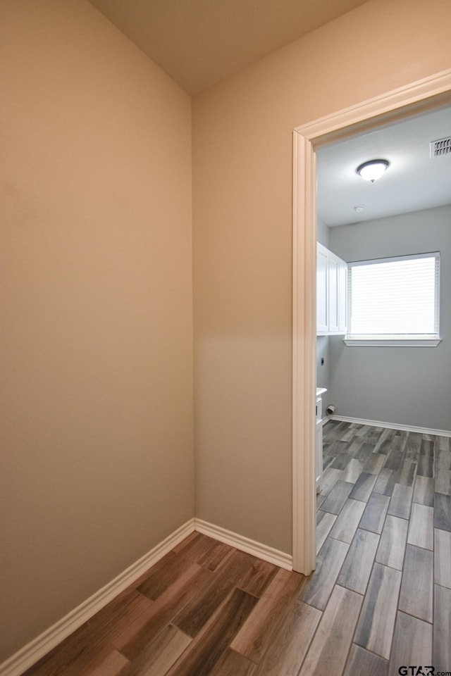 hall featuring visible vents, baseboards, and wood finished floors