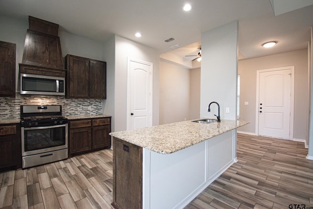 kitchen with a sink, appliances with stainless steel finishes, light wood-type flooring, decorative backsplash, and light stone countertops