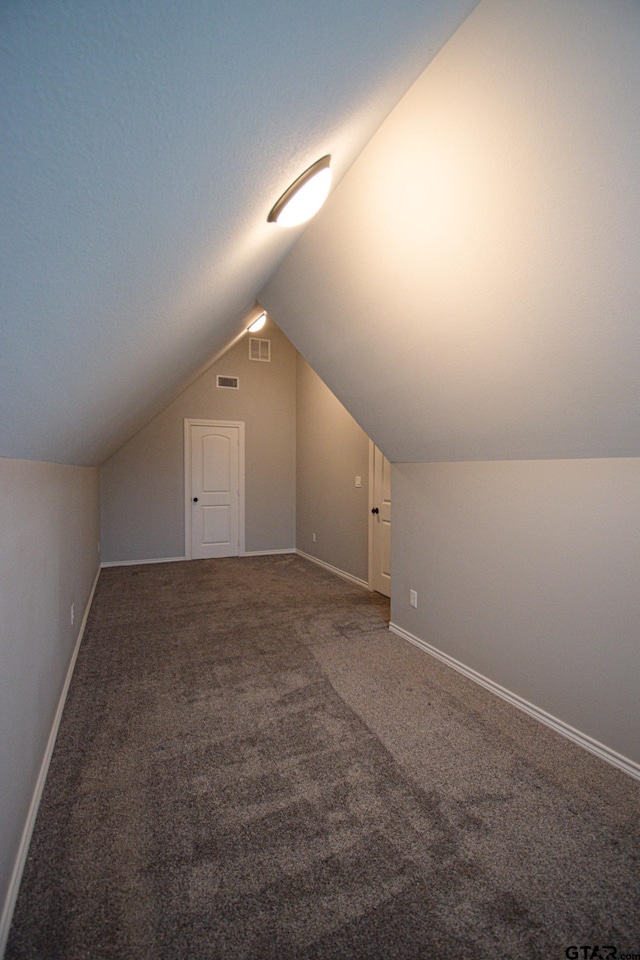 additional living space featuring lofted ceiling, visible vents, dark carpet, and baseboards