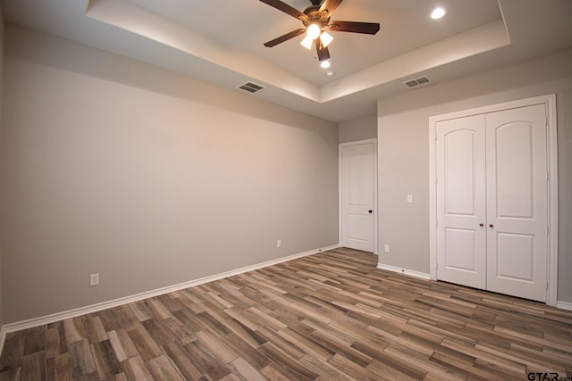 unfurnished bedroom featuring dark wood-style floors, a raised ceiling, visible vents, and baseboards