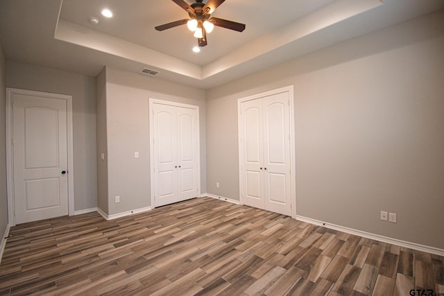 unfurnished bedroom with a tray ceiling, dark wood-type flooring, visible vents, and baseboards