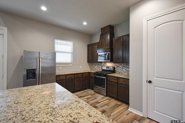 kitchen featuring light stone countertops, tasteful backsplash, stainless steel appliances, and light wood-style floors