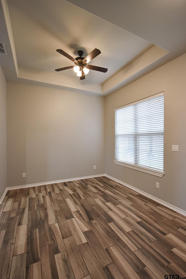 spare room featuring baseboards, a tray ceiling, and dark wood-type flooring