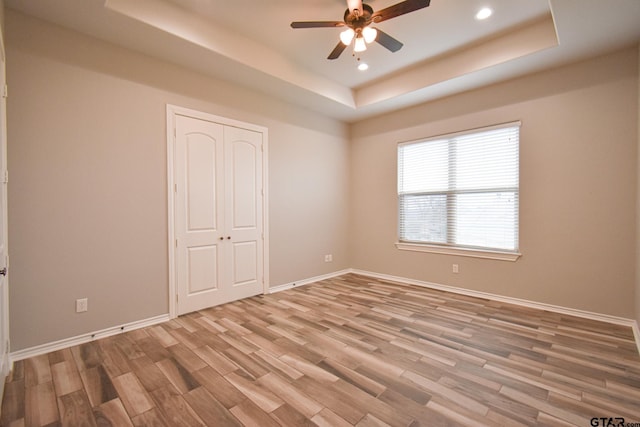 unfurnished bedroom with a tray ceiling, recessed lighting, ceiling fan, wood finished floors, and baseboards