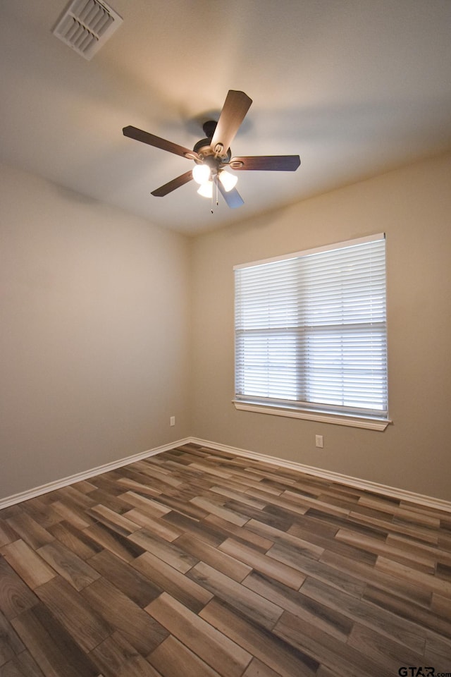 spare room with dark wood-style floors, a ceiling fan, visible vents, and baseboards