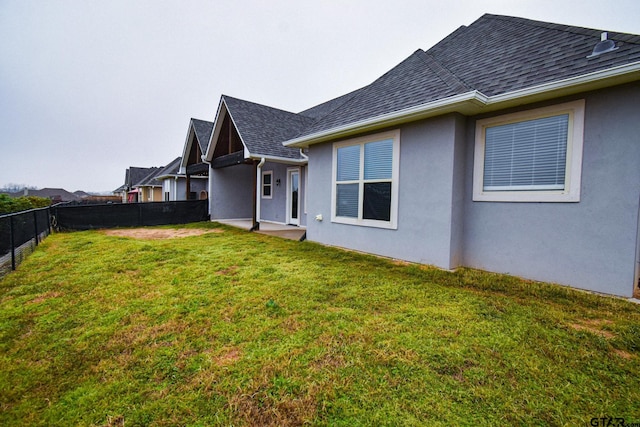 exterior space with a yard, a fenced backyard, stucco siding, and roof with shingles