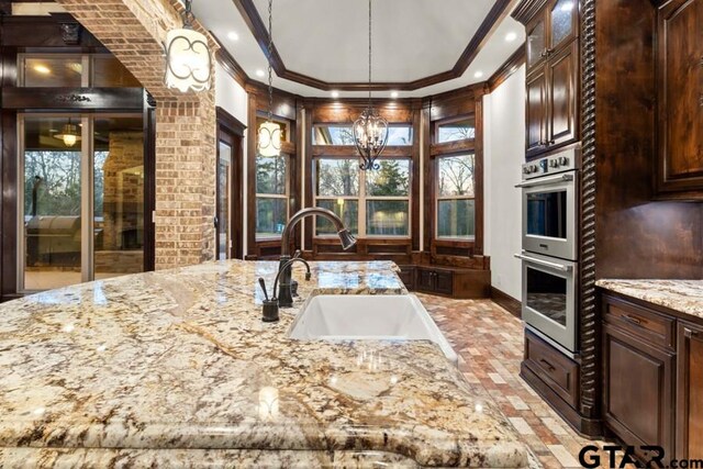 kitchen with light stone counters, a notable chandelier, sink, ornamental molding, and double oven