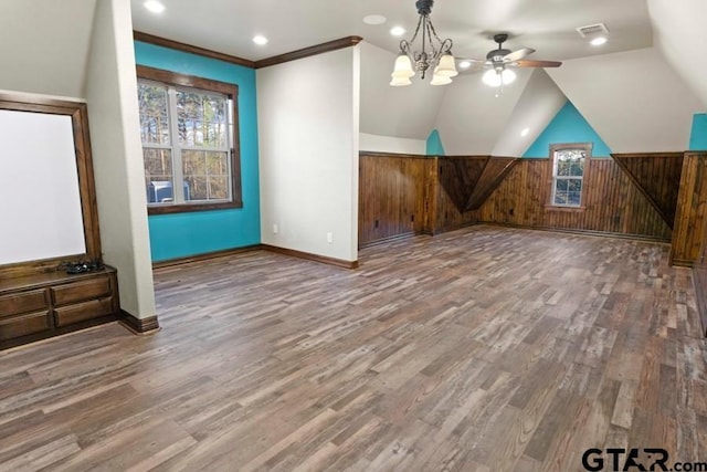 bonus room with hardwood / wood-style floors, ceiling fan with notable chandelier, wood walls, and lofted ceiling