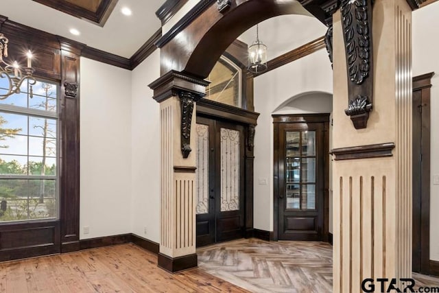 foyer featuring a chandelier, light parquet floors, crown molding, ornate columns, and french doors