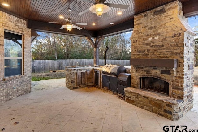 view of patio with ceiling fan, an outdoor stone fireplace, and exterior kitchen