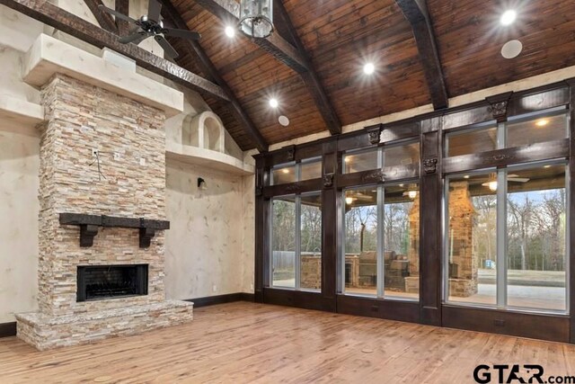 unfurnished living room with a stone fireplace, beam ceiling, high vaulted ceiling, hardwood / wood-style flooring, and wooden ceiling