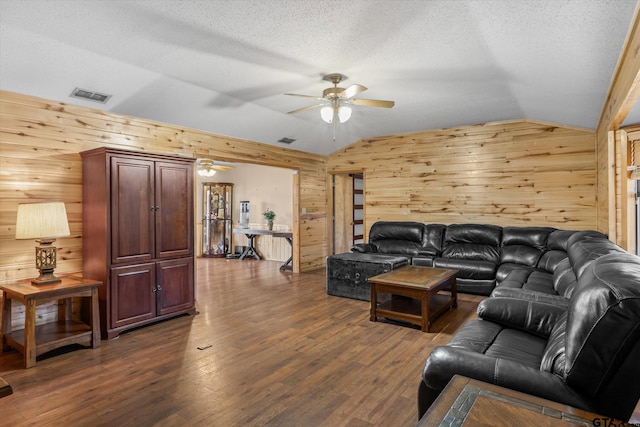 living room featuring lofted ceiling, wooden walls, dark wood-style floors, and visible vents