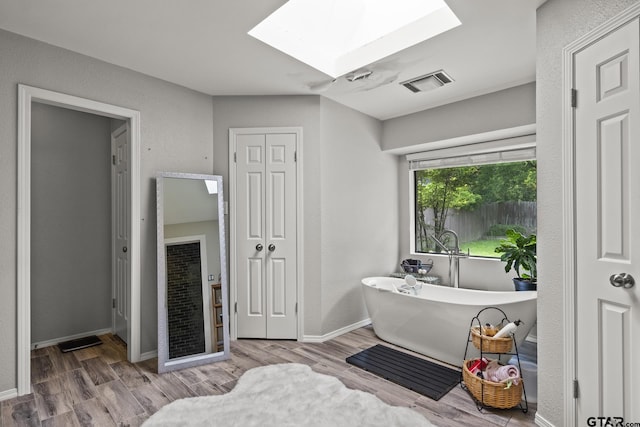 bathroom with a skylight, a bathing tub, and hardwood / wood-style flooring