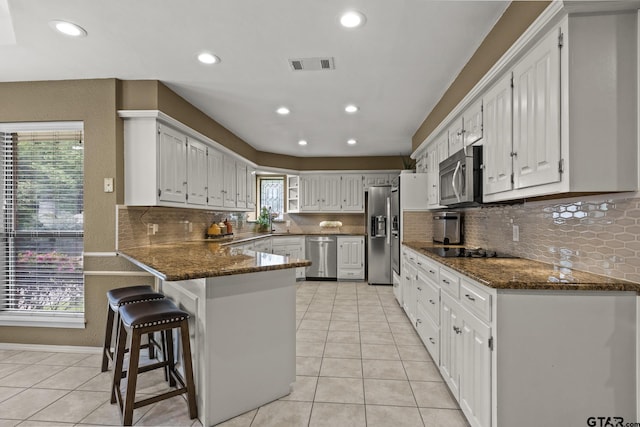 kitchen with white cabinetry, stainless steel appliances, kitchen peninsula, and dark stone counters