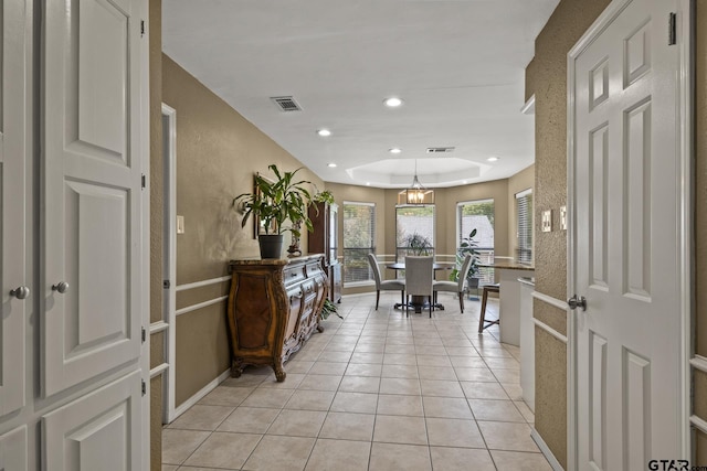 interior space with light tile patterned flooring, a tray ceiling, and a chandelier