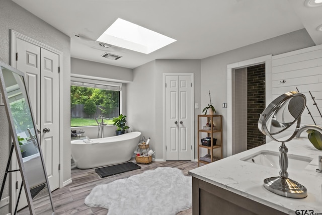 bathroom with vanity, a skylight, hardwood / wood-style floors, and a bath