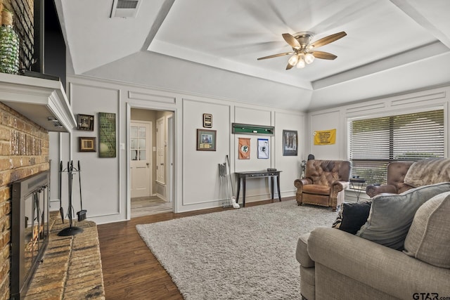 living room featuring ceiling fan, dark hardwood / wood-style flooring, a raised ceiling, and a brick fireplace