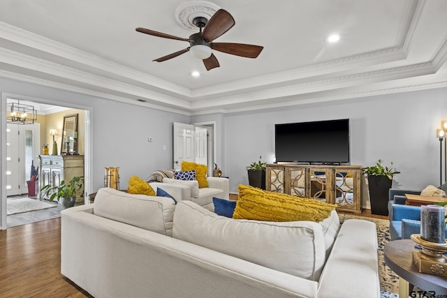 living room featuring ornamental molding, wood-type flooring, ceiling fan with notable chandelier, and a raised ceiling