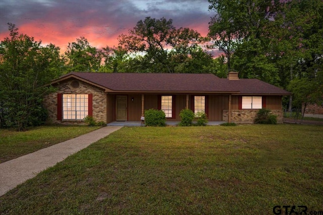 ranch-style home with a chimney, brick siding, board and batten siding, a lawn, and a porch