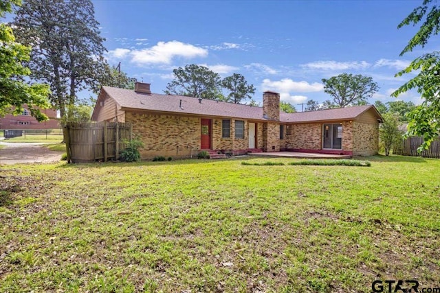 rear view of property with fence, a chimney, brick siding, a patio area, and a yard