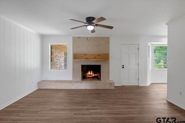 unfurnished living room featuring ornamental molding, a brick fireplace, wood finished floors, baseboards, and a ceiling fan