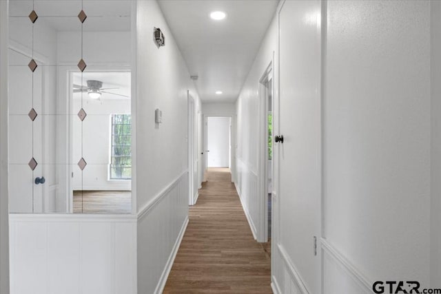 hallway with recessed lighting, wainscoting, a decorative wall, and wood finished floors