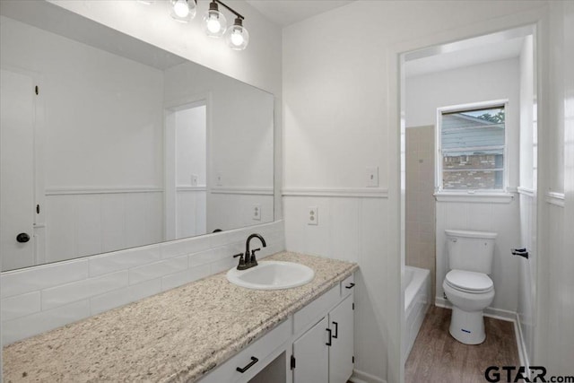 bathroom with a wainscoted wall, toilet, wood finished floors, and vanity