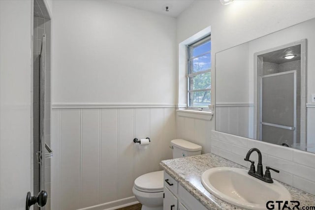 bathroom with an enclosed shower, toilet, wainscoting, and vanity