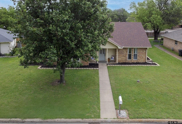 view of front of home with covered porch, a shingled roof, a front lawn, and brick siding