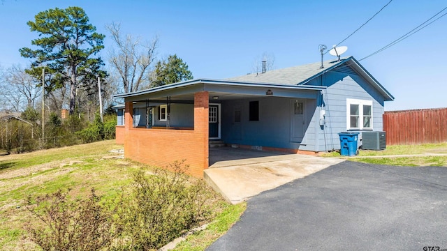 bungalow-style home with a front lawn, driveway, fence, cooling unit, and a carport