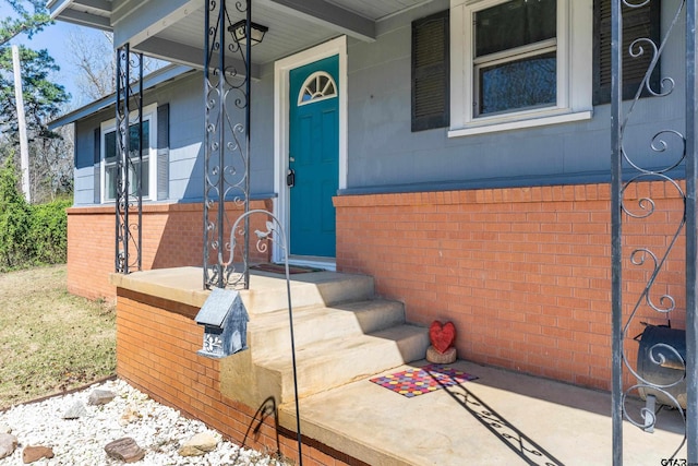 view of exterior entry featuring a porch and brick siding