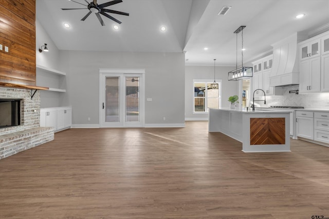 kitchen with white cabinetry, a fireplace, an island with sink, decorative light fixtures, and custom range hood