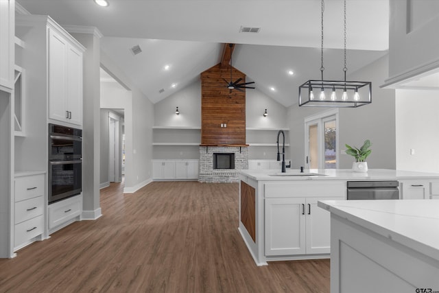 kitchen featuring a brick fireplace, black double oven, sink, white cabinetry, and pendant lighting