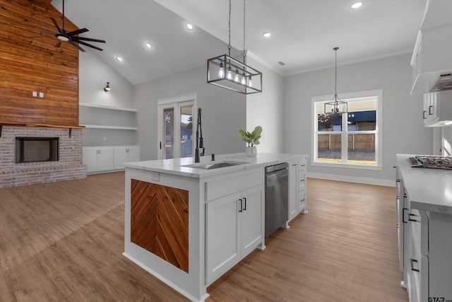 kitchen featuring a center island with sink, a brick fireplace, appliances with stainless steel finishes, white cabinetry, and pendant lighting