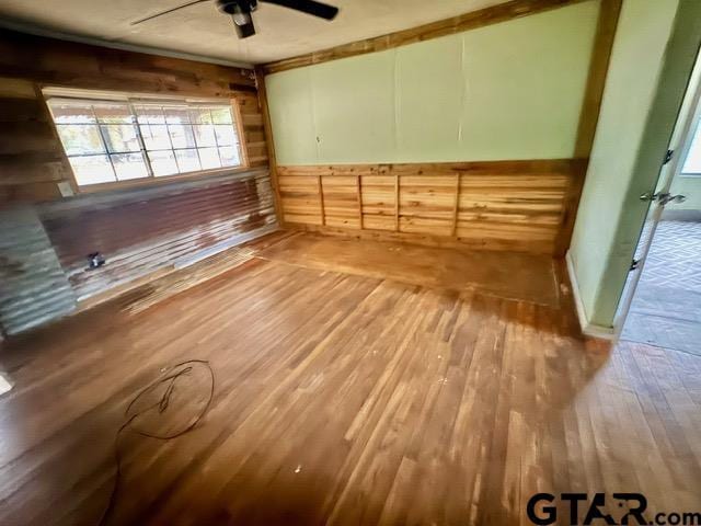 spare room featuring hardwood / wood-style floors, ceiling fan, ornamental molding, and wood walls