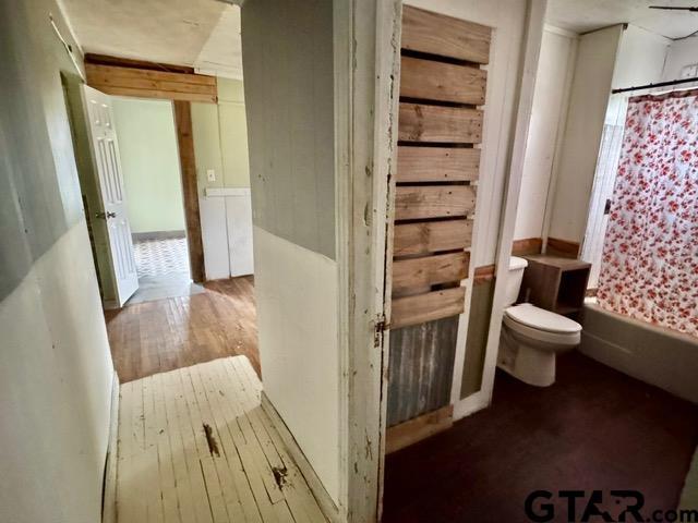 bathroom with toilet, wood-type flooring, and shower / tub combo with curtain