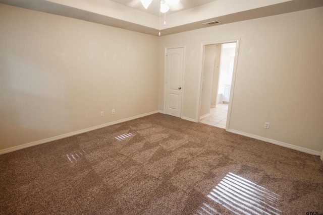 spare room with ceiling fan, light colored carpet, and a tray ceiling