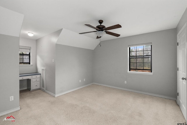 unfurnished bedroom featuring built in desk, light colored carpet, ceiling fan, and lofted ceiling